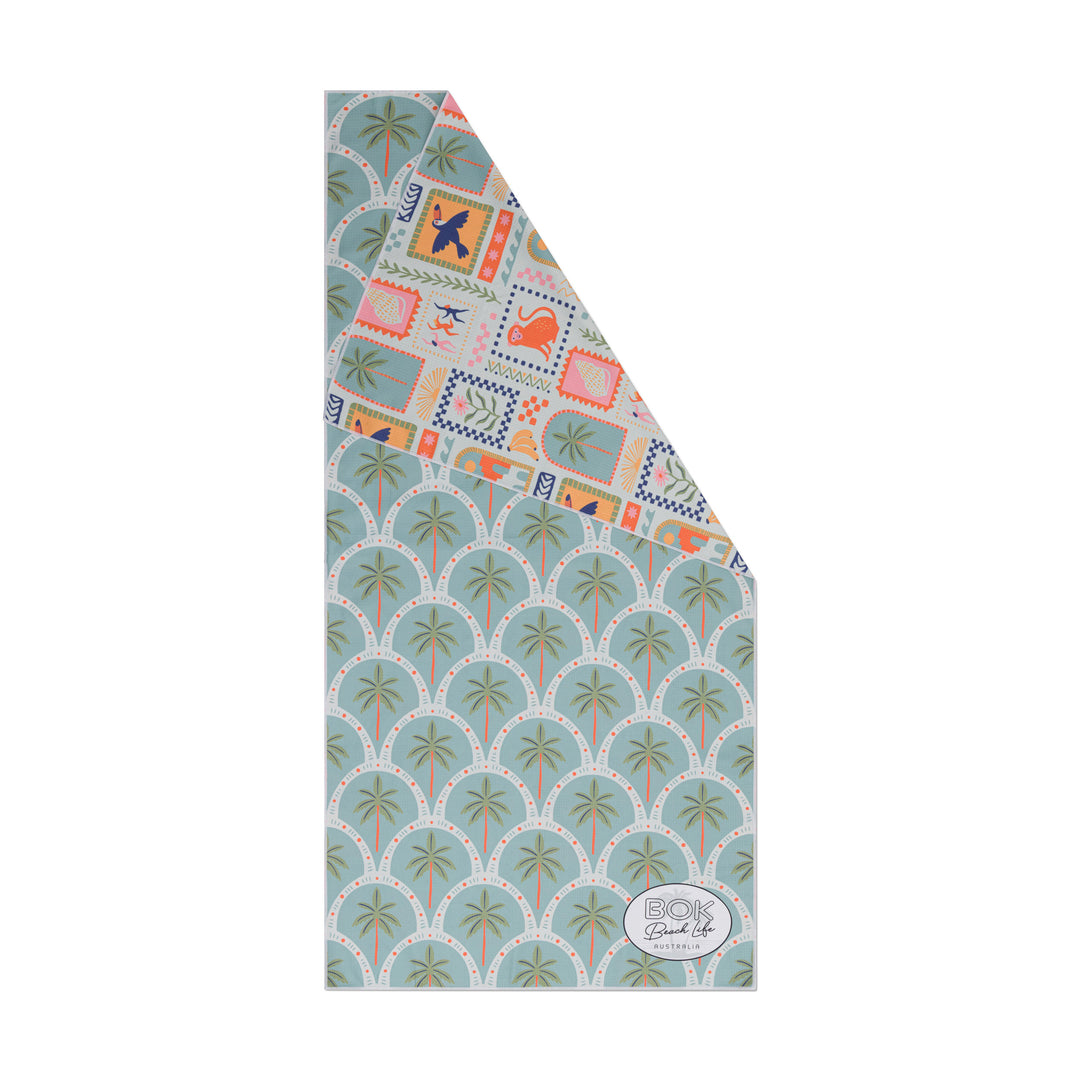 Folded sand free waffle weave fabric towel showing reverse tropical patterns on a white background 