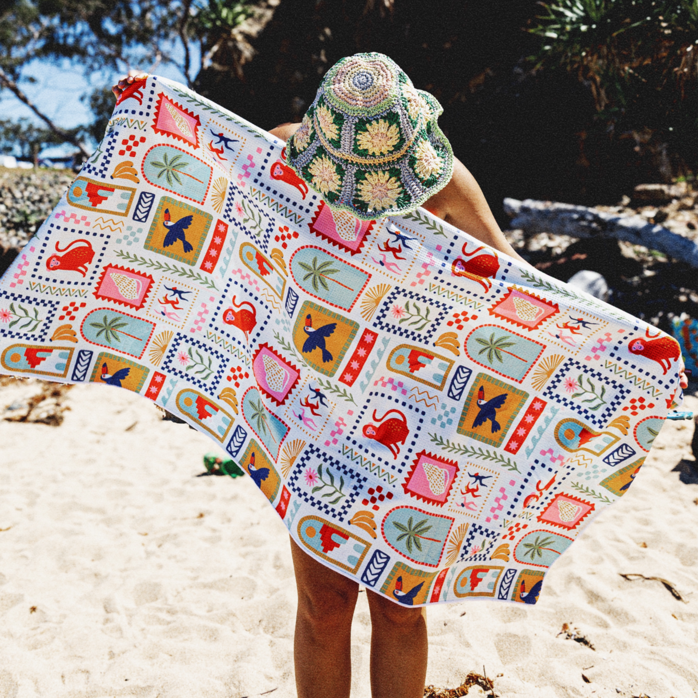 Lady holding a colorful patterned sand free towel wearing a hat on white sand beach
