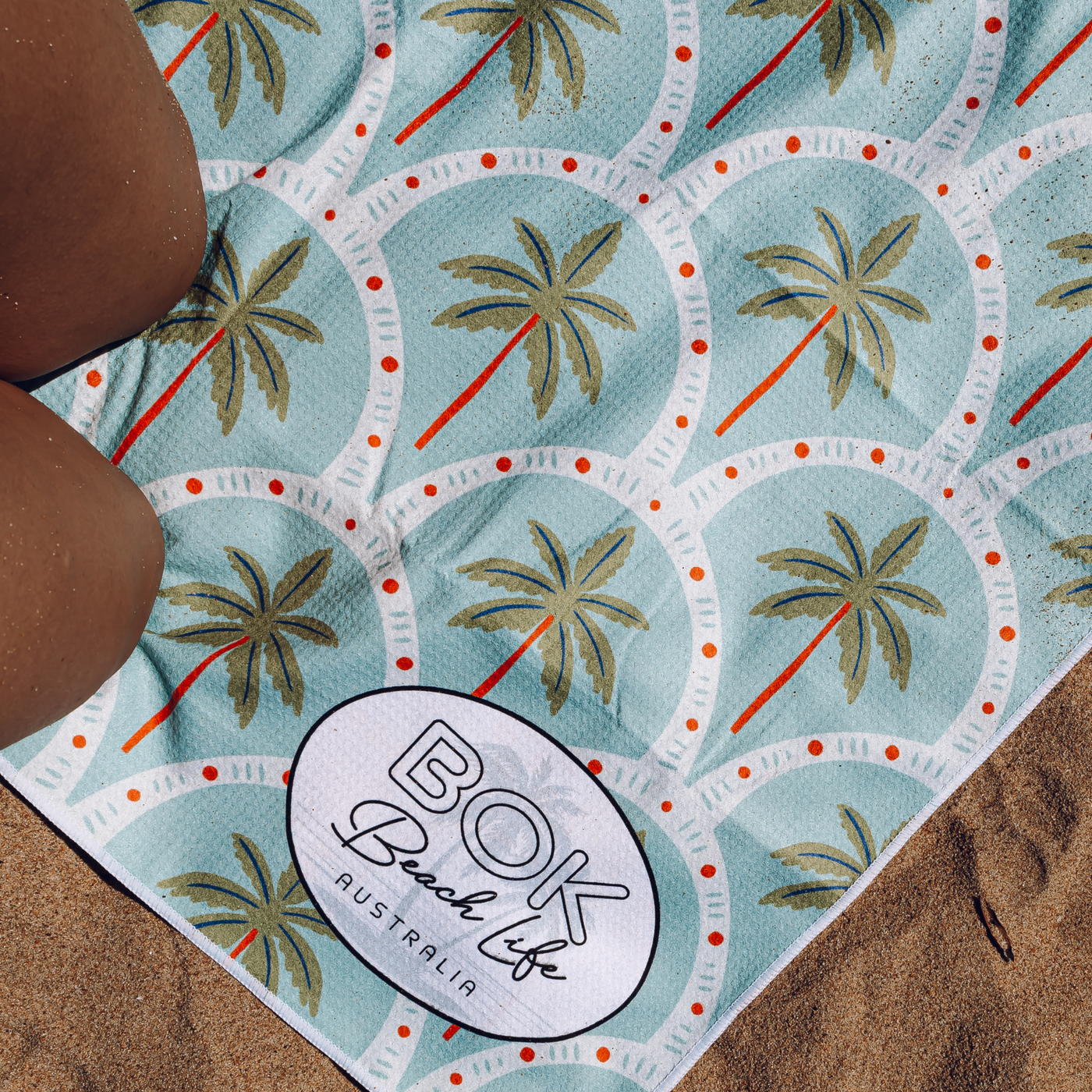 Sand free Beach towel with palm tree pattern and 'BOK Beach Life Australia' logo on sand.