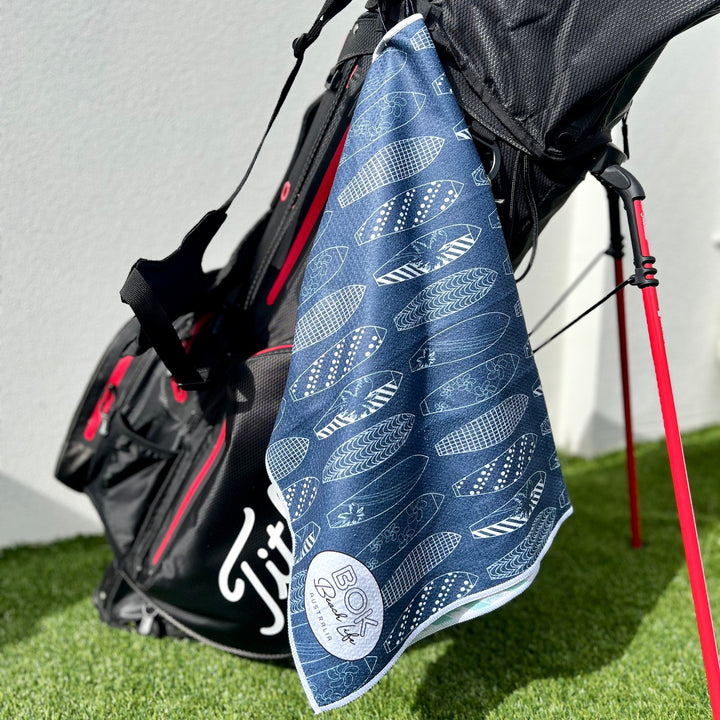 Golf towel with navy blue surfboard pattern hanging from a golf bag on grass