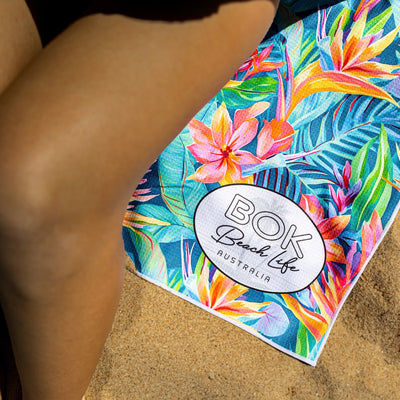 Colorful tropical patterned birds of paradise beach towel'BOK Beach Life Australia' logo on sand.