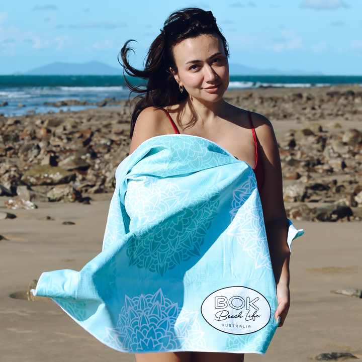 Woman on a beach holding a blue towel with &