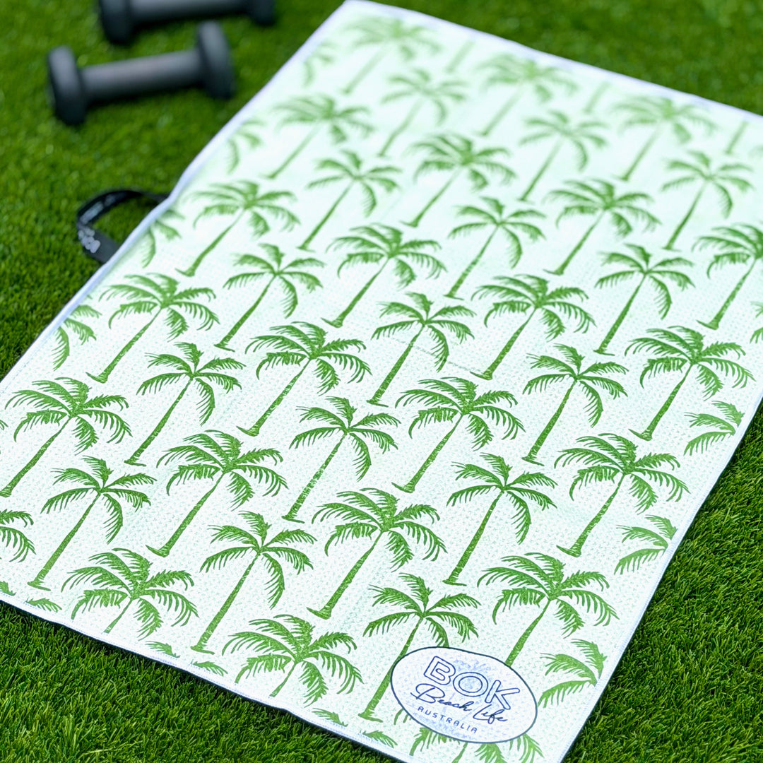 Green waffle weave handy towel with green palm tree pattern on grass