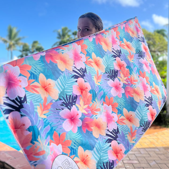 Girl  holding a colorful tropical floral sand free towel with palm trees in the background