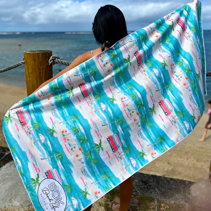 Person holding a colorful towel with beach-themed design by the sea