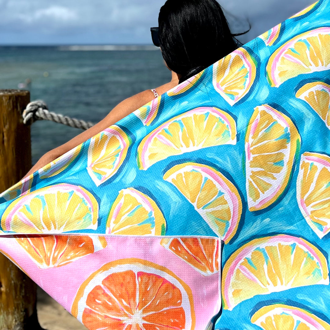 Lady standing by the ocean with a colorful beach towel towel featuring lemon slices