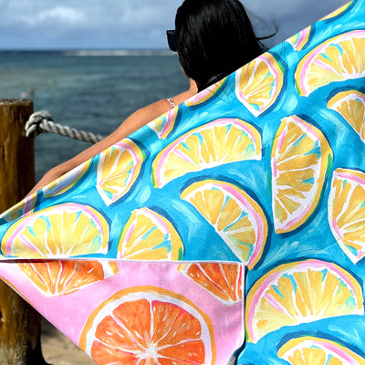 Lady standing by the ocean with a colorful beach towel towel featuring lemon slices