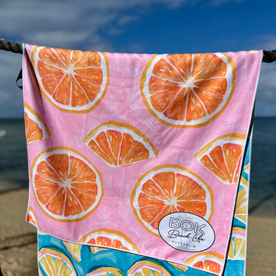 Pink towel with orange fruit slice pattern hanging on a rope by beach.