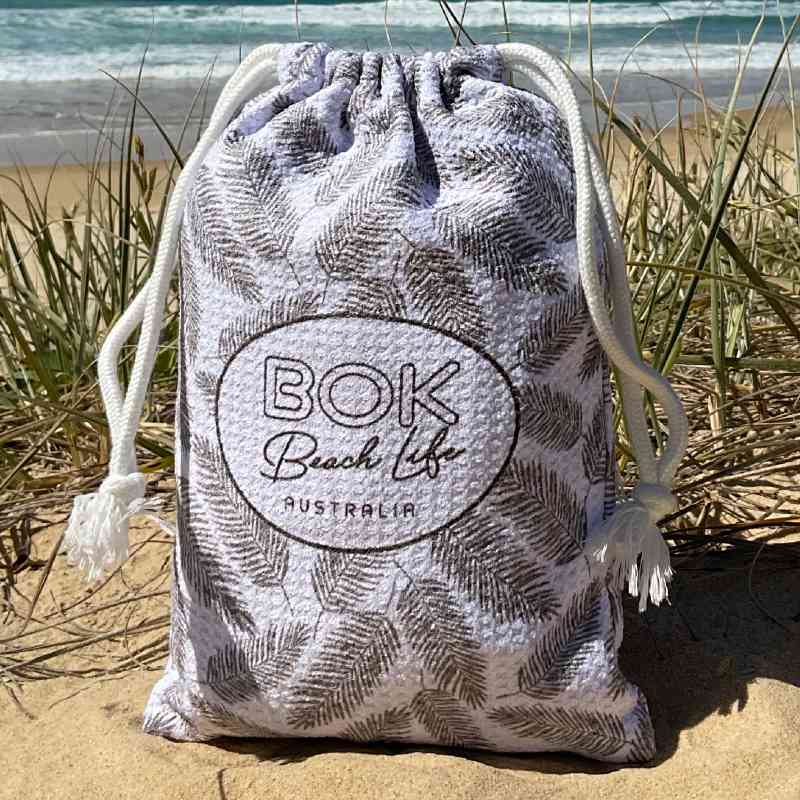 Coastal Luxe Design Sand free beach towel in compact microfibre waffle fabric carry bag. Design features feathers and chevron pattern.